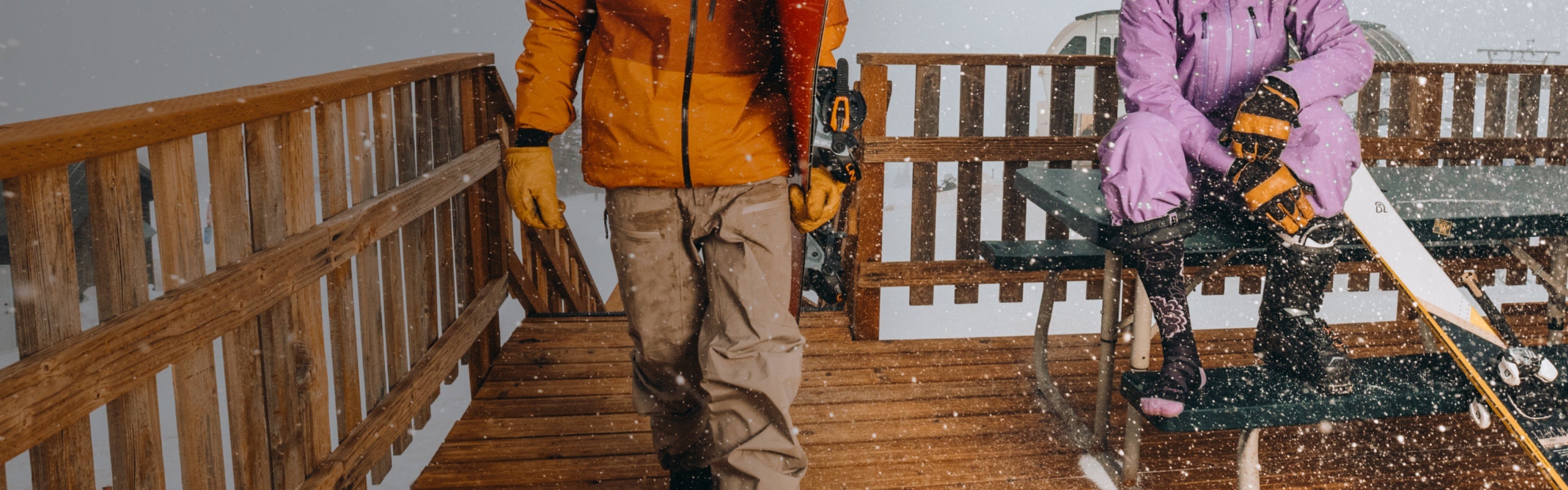 A skier and snowboarder at a top-of-the-mountain lodge on a snowy day in Darn Tough socks