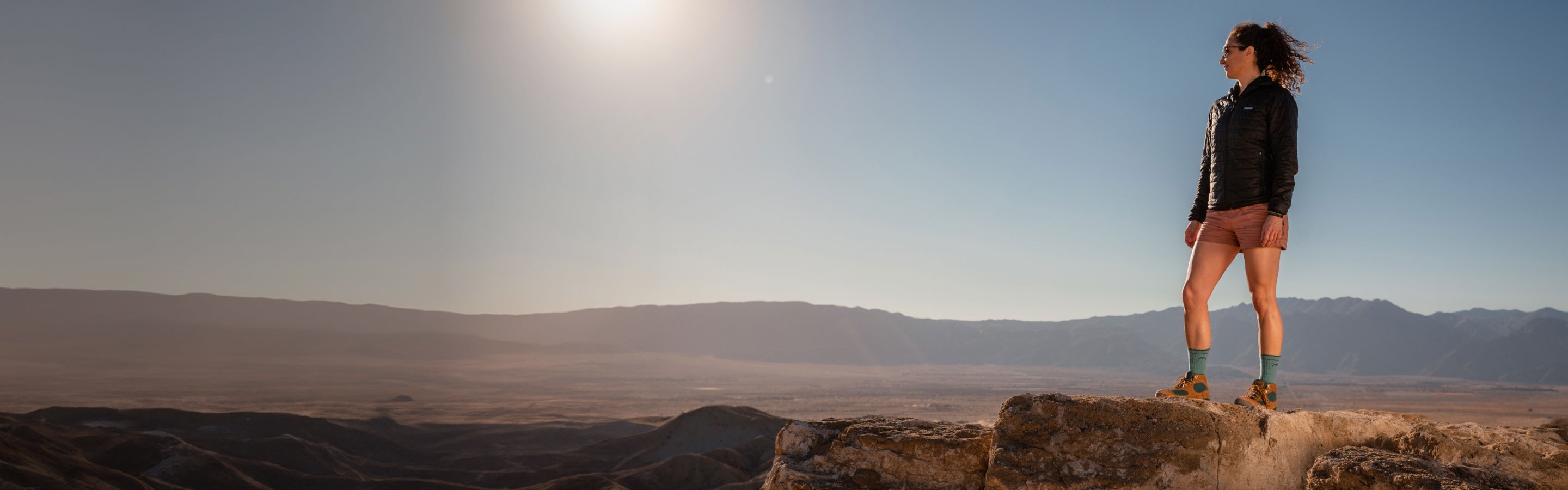 Woman wearing Darn Tough hiking socks standing on a dramatic outlook