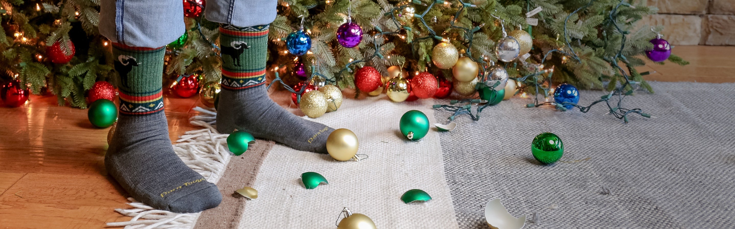 Feet wearing Darn Tough socks standing by a downed Christmas tree and broken ball ornaments